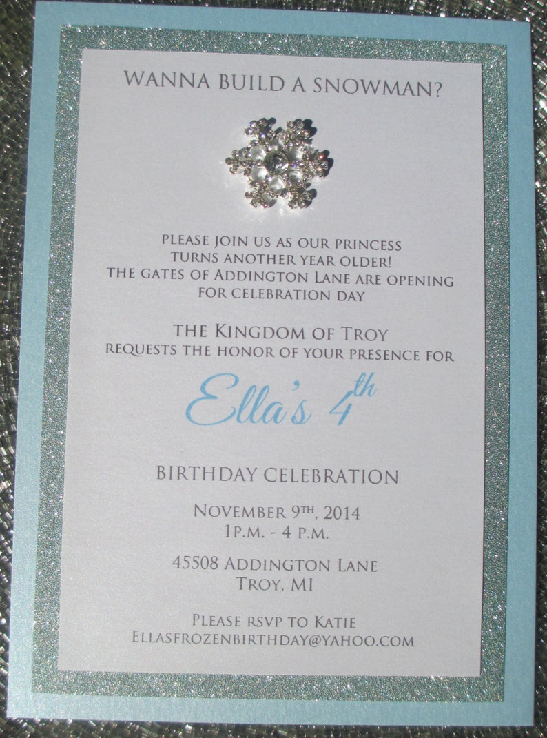 May include: A light blue invitation with silver glitter trim. The invitation is for a 4th birthday party for a girl named Ella. The invitation features a snowflake with rhinestones and the text "Wanna build a snowman?" at the top. The invitation includes the date, time, and location of the party. The text "Ella's 4th Birthday Celebration" is in a larger font size than the rest of the text.