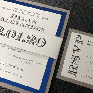 May include: A grey and blue invitation with a white inner layer. The invitation is for a Bar Mitzvah for Dylan Alexander on 1st February 2020. The RSVP card is grey with black text and asks guests to RSVP by 4th January 2020.