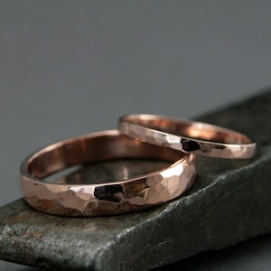 May include: Two rose gold hammered wedding bands. The wider band is on top of the thinner band.