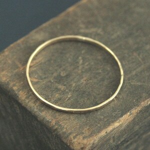 May include: A thin, circular gold ring with a smooth, polished finish. The band is uniform in thickness and features a simple, continuous design without any gemstones, engravings, or additional decorative elements on its surface.
