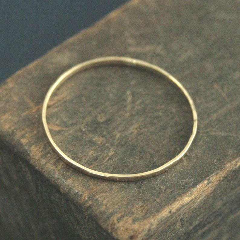 May include: A thin, circular gold ring with a smooth, polished finish. The band is uniform in thickness and features a simple, continuous design without any gemstones, engravings, or additional decorative elements on its surface.