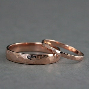 May include: Two rose gold wedding bands with a hammered finish. The wider band has a more pronounced hammered texture.
