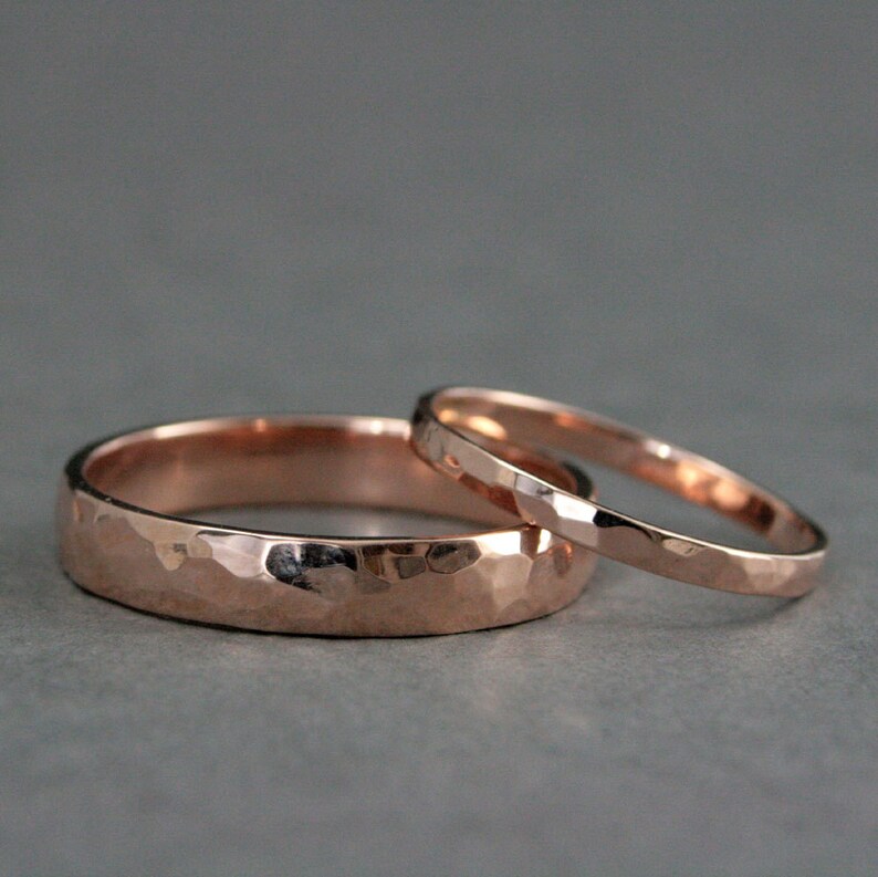 May include: Two rose gold wedding bands with a hammered finish. The wider band has a more pronounced hammered texture.