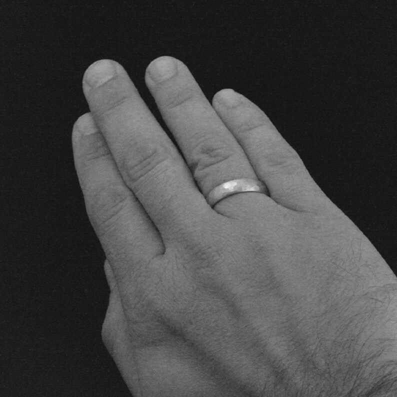 May include: A close-up of a hand wearing a silver wedding band.