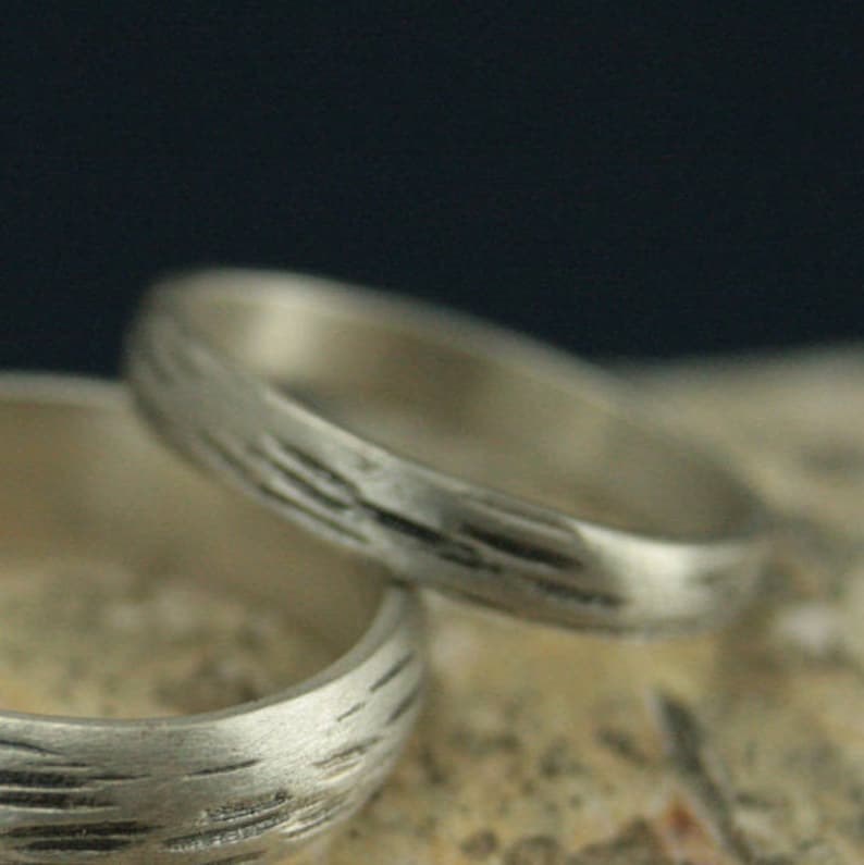 May include: Two silver wedding bands with a textured, wood-like pattern.