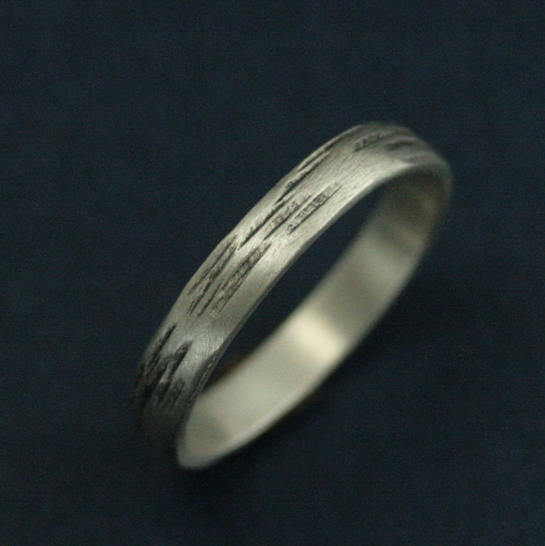 May include: A silver band ring with a textured, brushed finish. The ring has a simple, modern design.