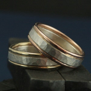 May include: Two wedding bands with a hammered finish. The top band is silver with a rose gold inlay. The bottom band is silver with a yellow gold inlay.