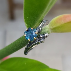 May include: A silver ring with a blue gemstone set in gold. The ring is designed to look like a branch with leaves.