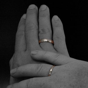 May include: Two hands with wedding bands on their ring fingers. The bands are both gold and have a hammered texture.