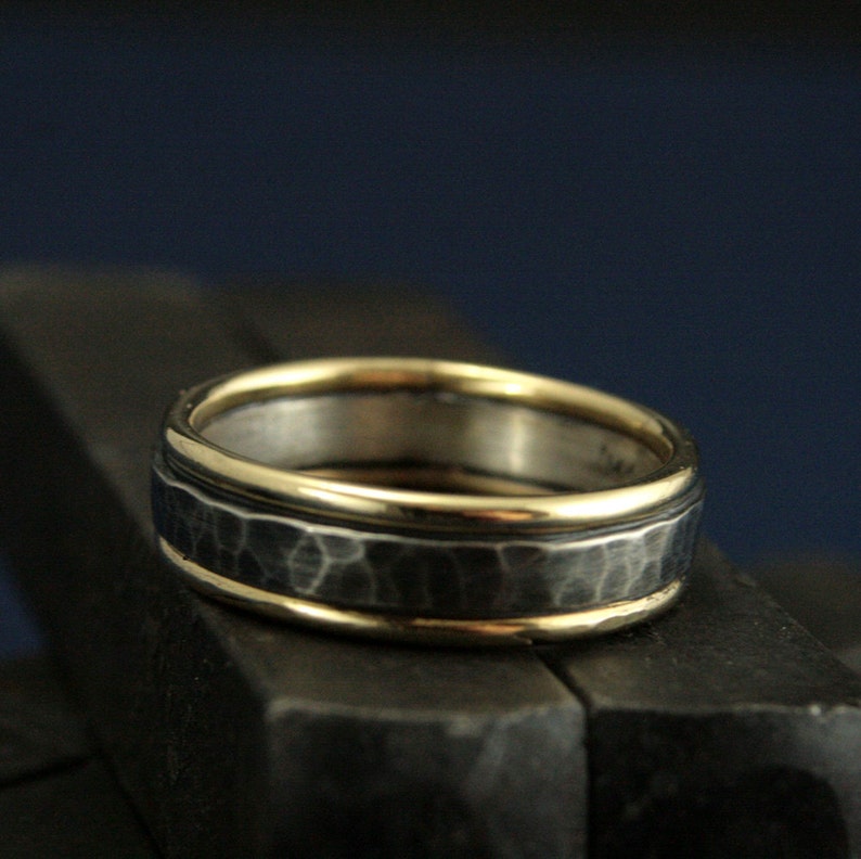 May include: A silver band with a hammered texture and two thin gold bands around the edge.