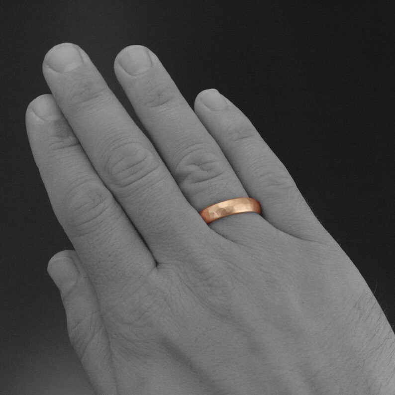 May include: A close-up of a hand wearing a hammered rose gold wedding band.