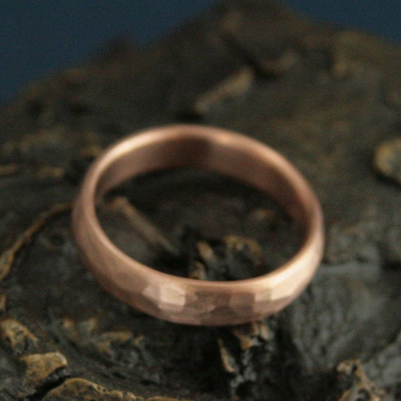 May include: A hammered copper ring with a rounded profile. The ring has a textured surface and a warm, metallic color.