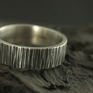 May include: Close-up of a silver ring with a textured, vertical lined pattern. The ring has a wide band and a matte finish. The ring is likely made of sterling silver and is a piece of jewelry.