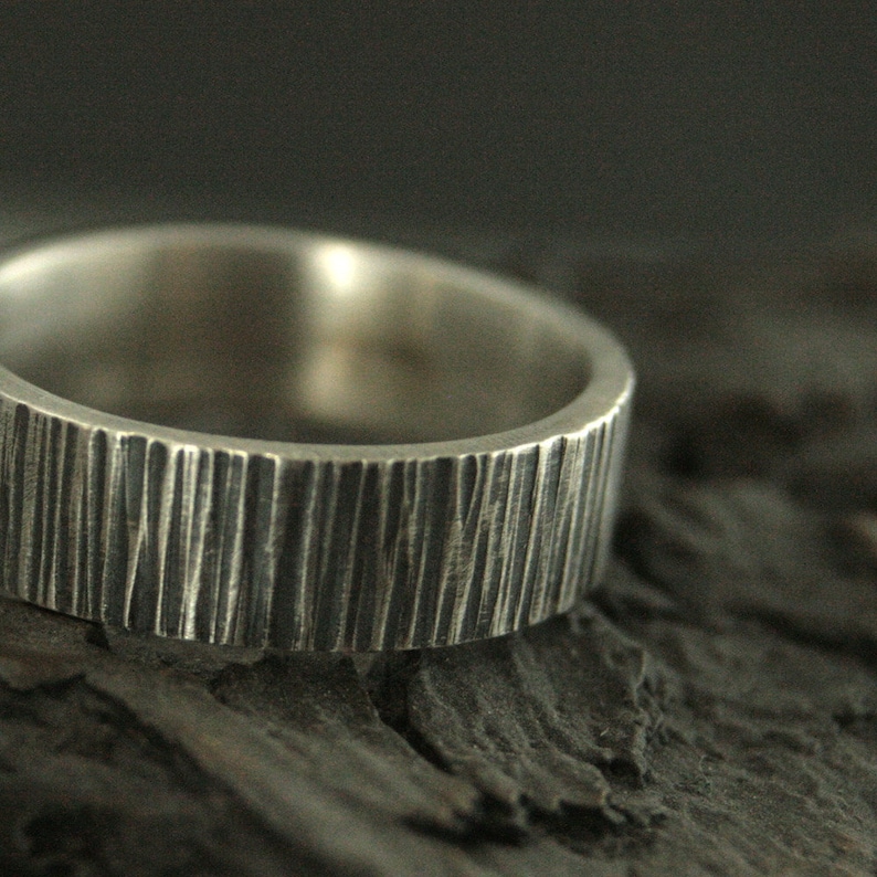 May include: Close-up of a silver ring with a textured, vertical lined pattern. The ring has a wide band and a matte finish. The ring is likely made of sterling silver and is a piece of jewelry.