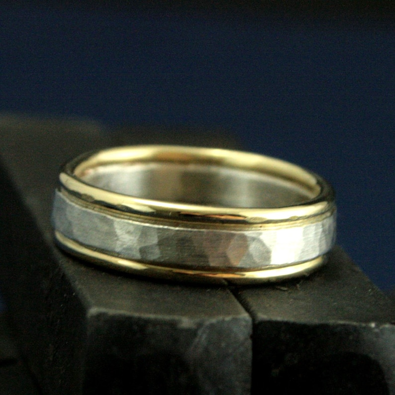 May include: A silver band with a hammered texture and two thin gold bands around the edge.