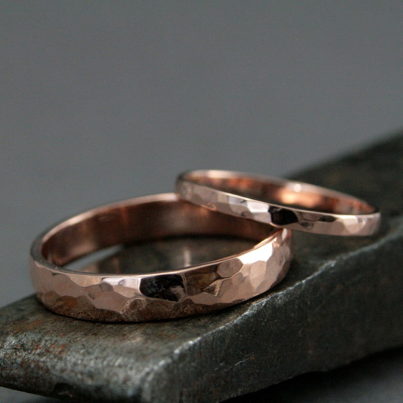 May include: Two rose gold hammered wedding bands. The wider band is on top of the thinner band.