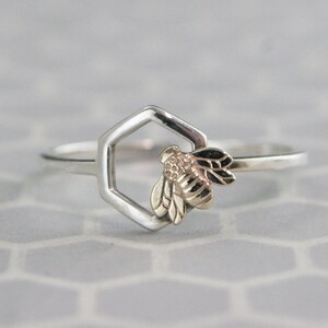 May include: A silver ring with a gold bee design inside a hexagon shape.