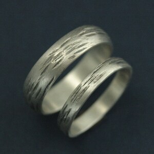 May include: Two silver wedding bands with a textured, brushed finish. The bands are stacked on top of each other.