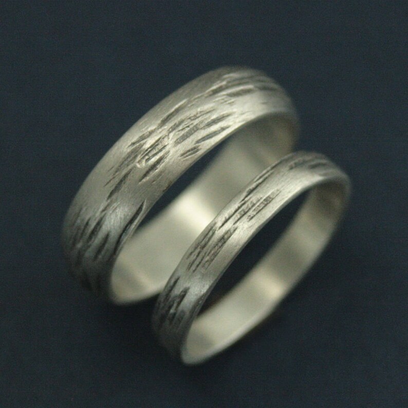 May include: Two silver wedding bands with a textured, brushed finish. The bands are stacked on top of each other.