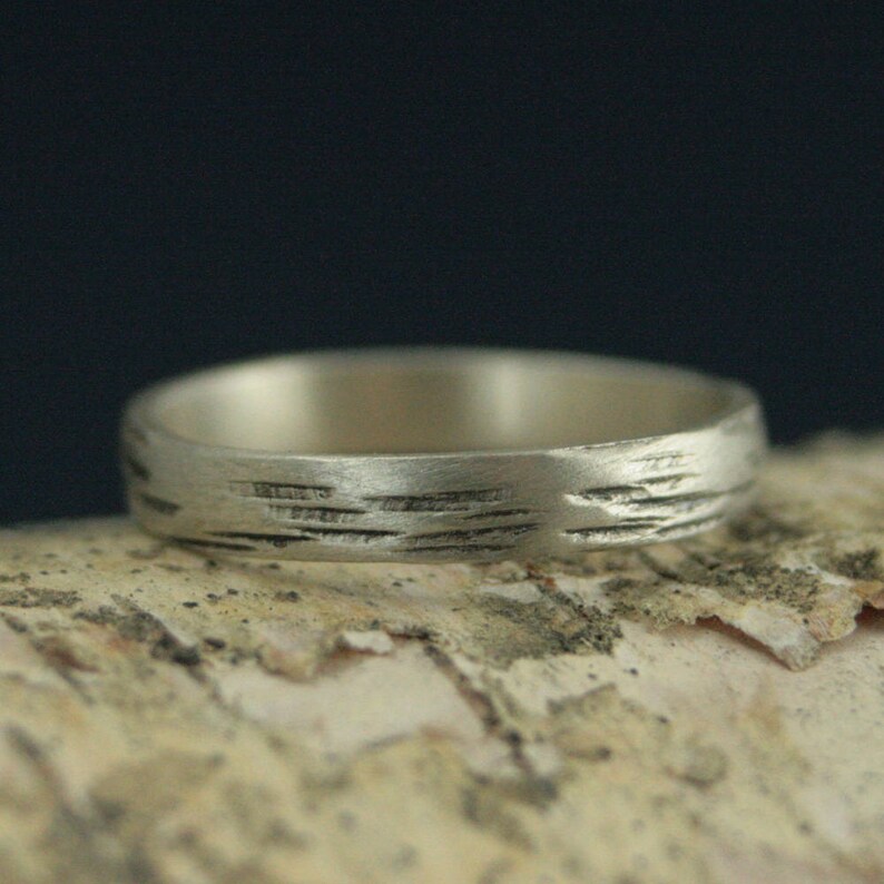 May include: A silver band ring with a textured surface that resembles the bark of a tree.