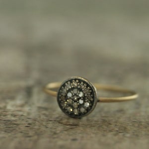 May include: A delicate gold band ring with a round, pave-set diamond center. The diamonds are set in a silver bezel.