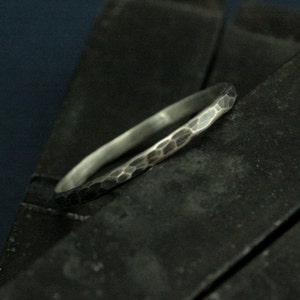 May include: A silver ring with a hammered texture. The ring is thin and has a polished finish.