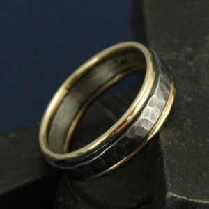 May include: A hammered silver band with a double band of gold around the edge.