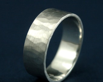 Aliança de casamento em ouro branco martelado. O diabo está nos detalhes. Anel em formato de charuto com borda plana. Interior polido, exterior fosco e martelado. 6 mm de largura.