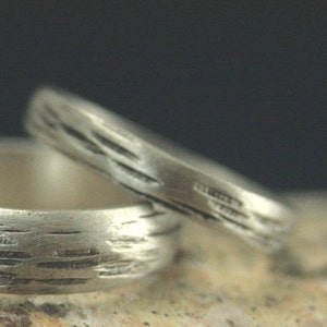 May include: Two silver rings with a textured, wood-like pattern. The rings are stacked on top of each other.