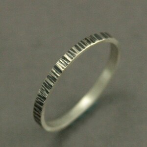 May include: A silver ring with a textured, bark-like pattern around the band. The ring has a simple, elegant design, perfect for everyday wear. The ring is shown against a gray background.