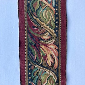 May include: Close-up of a burgundy and black tapestry fabric with a repeating pattern of stylized leaves and vines. The fabric has a gold thread woven into the design.