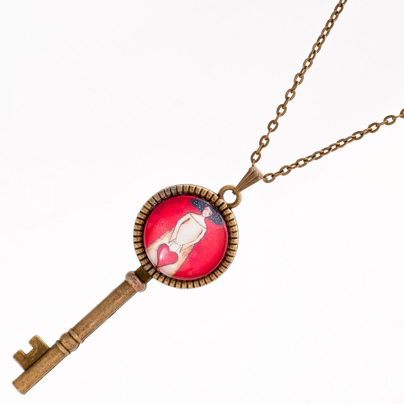 May include: A bronze key necklace with a round pendant featuring a woman in a red dress holding a heart. The pendant is surrounded by a decorative bronze frame.