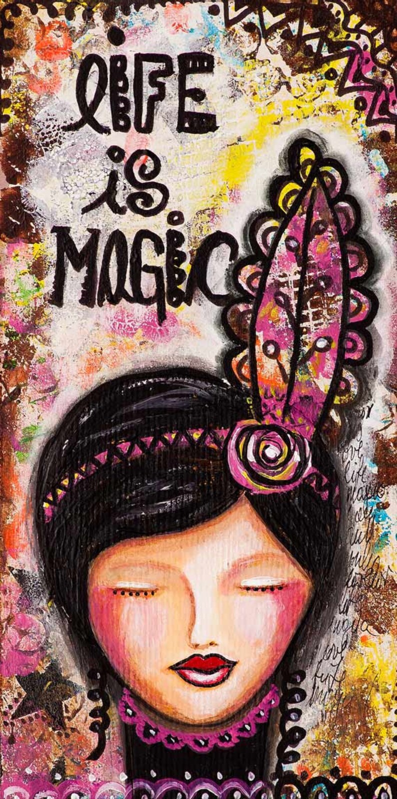 May include: A colorful painting of a woman with closed eyes and a pink flower in her hair. The text "Life is Magic" is written in black paint above her head.