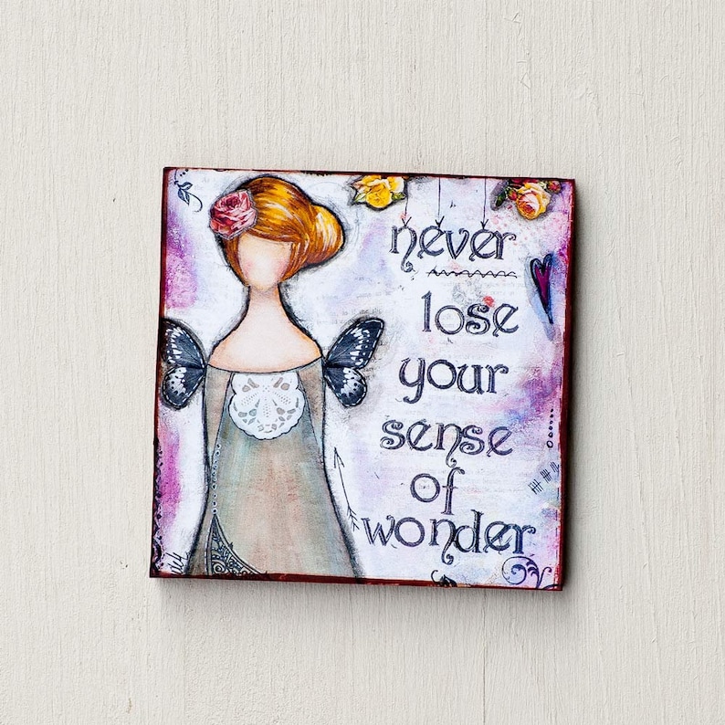 K&ouml;nnte beinhalten: Ein farbenfrohes Gem&auml;lde auf einer Holzleinwand mit einem M&auml;dchen mit roten Haaren und Fl&uuml;geln. Das Gem&auml;lde tr&auml;gt den Text "never lose your sense of wonder".