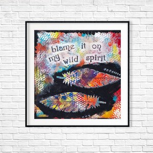 Puede incluir: Una impresi&oacute;n de arte enmarcada en blanco y negro con un fondo abstracto colorido y dos plumas coloridas. El texto "blame it on my wild spirit" est&aacute; escrito en negro en la impresi&oacute;n.