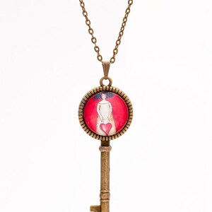 May include: A gold key necklace with a round pendant featuring a woman holding a red heart. The pendant is set against a red background.