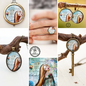 May include: A set of jewelry featuring a key pendant necklace, a ring, and earrings. The pendant, ring, and earrings all feature a round, glass-like charm with a painted image of a woman with long hair and the text "be brave listen to intuition dream big embrace passion joy creativity and love".