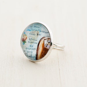 May include: Silver ring with a round glass cabochon featuring a vintage-style image and the text "Be brave, listen to intuition, dream big, embrace passion, joy, creativity, love".