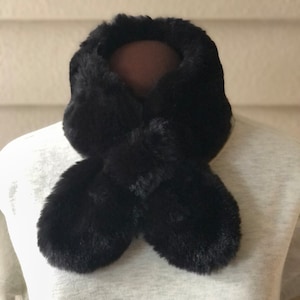 May include: A black faux fur neck warmer with a fluffy texture. The neck warmer is folded in half and tied in a knot at the front.