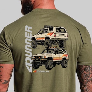 May include: Olive green t-shirt featuring a graphic of two off-road Toyota 4Runner SUVs. The design includes the word "4Runner" in white and the text "OGSUV" in orange. The vehicles are white with orange and red stripes.