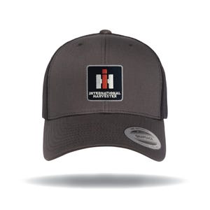 May include: A charcoal gray trucker hat with a curved brim and mesh back. The front features a square patch with the words "INTERNATIONAL HARVESTER" below a logo with red and white vertical bars.