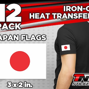 May include: A pack of 12 iron-on heat transfers featuring the Japanese flag. Each transfer is 3 inches by 2 inches. The image shows a black t-shirt with a Japanese flag ironed on the sleeve. The text "IRON-ON HEAT TRANSFERS" and "JAPAN FLAGS" is visible in the image.