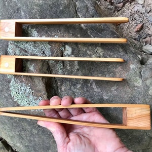 May include: Three wooden tongs of varying sizes, with a natural wood finish. The tongs are made of a single piece of wood and have a simple design.