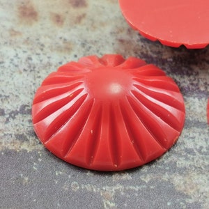 May include: Three red plastic cabochons with a sunburst design. The cabochons are approximately 1 inch in diameter.