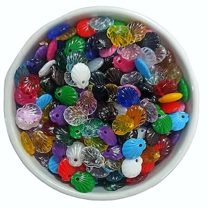 以下が含まれることがあります： カラフルなプラスチック製の貝殻の形をしたビーズが入ったボウル。ビーズは赤、青、緑、黄、紫の様々な色合いです。