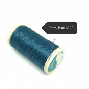 May include: A spool of petrol blue thread, color code 6093, is displayed against a white background. The thread is tightly wound around a white and cream-colored spool. A small piece of thread extends from the spool.
