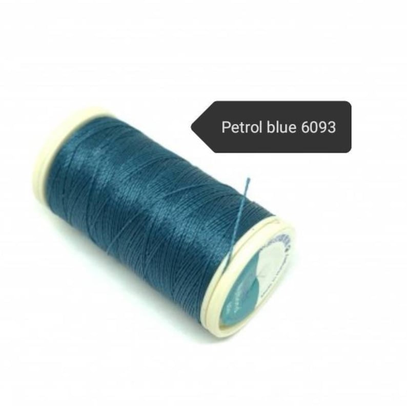 May include: A spool of petrol blue thread, color code 6093, is displayed against a white background. The thread is tightly wound around a white and cream-colored spool. A small piece of thread extends from the spool.