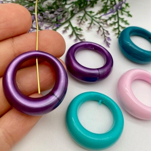 May include: Four colorful plastic rings in purple, teal, pink, and turquoise. The rings are smooth and glossy.