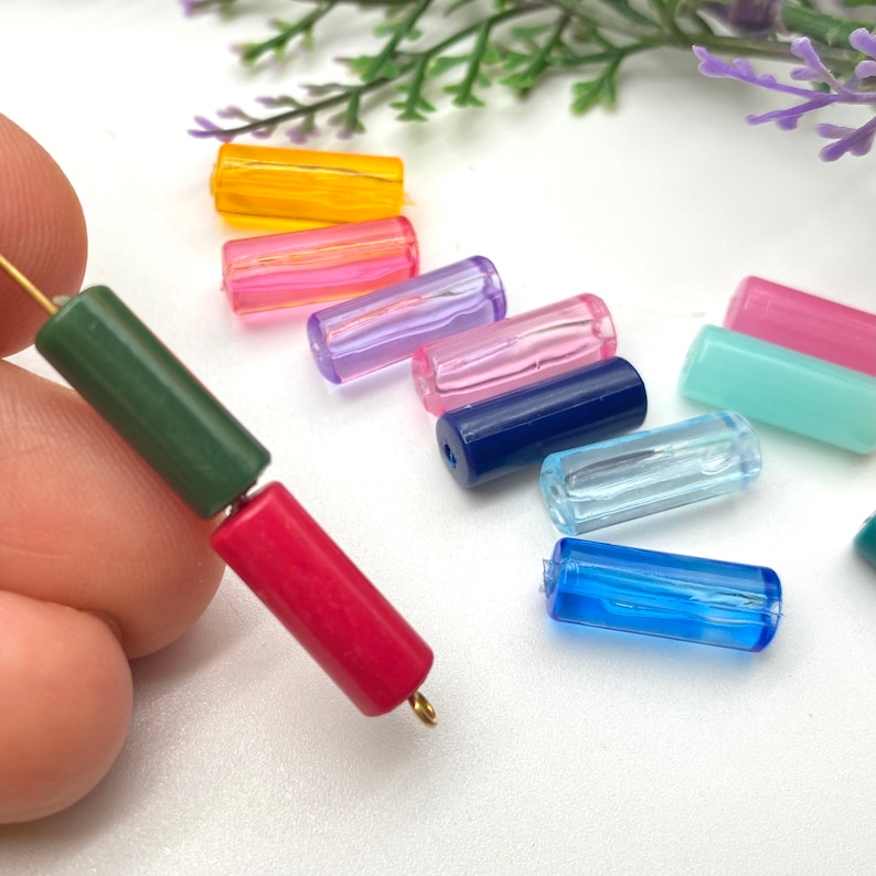 May include: Assortment of colorful glass beads in various shades of blue, green, pink, and yellow. The beads are cylindrical in shape and have a smooth, glossy finish.