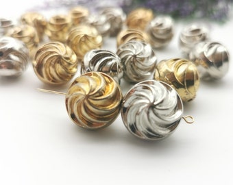 May include: A collection of gold and silver swirl-patterned beads. The beads are round and have a shiny finish.